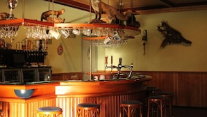 Un espace bar avec des tabourets, un comptoir, une étagère à verres et des têtes d’animaux fixées au mur.