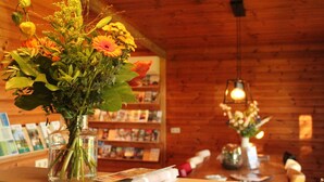 Un intérieur en bois, avec un vase en verre transparent contenant des fleurs, posé sur une table, le tout entouré d’étagères à livres.