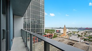 A high-rise building with a balcony, a view of a cityscape including a prominent tower, and a waterfront with a cruise ship. - Luxury Downtown Miami 501 First Rooftop Pool View (Miami)