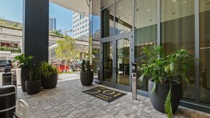 A hotel entrance with a glass door, potted plants, a doormat, and a parking lot in the background. - Luxury 2BR/2BA • Rooftop Pool • Downtown Miami (Miami)