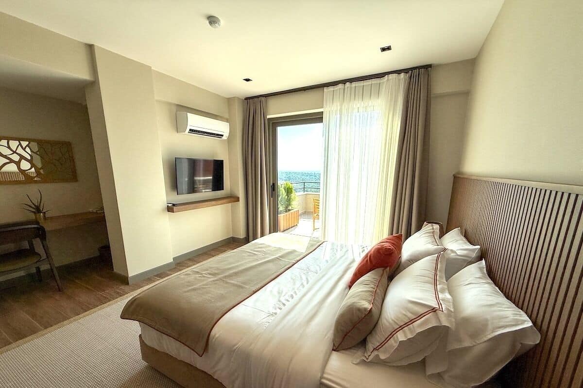 Un dormitorio con cama, televisor, ventana con cortinas y vistas al exterior.