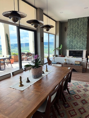 A spacious living area with a large wooden dining table, modern pendant lighting, and a fireplace. - Reya Kazdağları (Ayvacık)