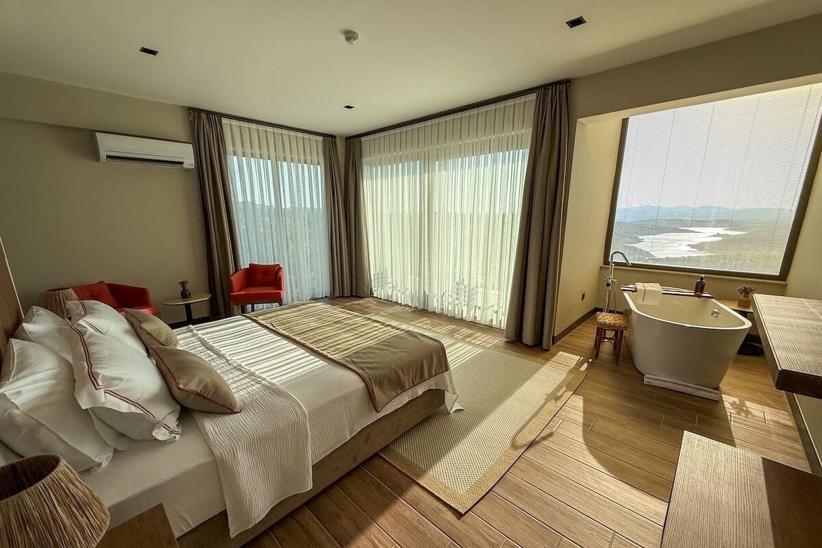 Habitación de hotel con una cama grande, una bañera, vista al océano y una silla roja.