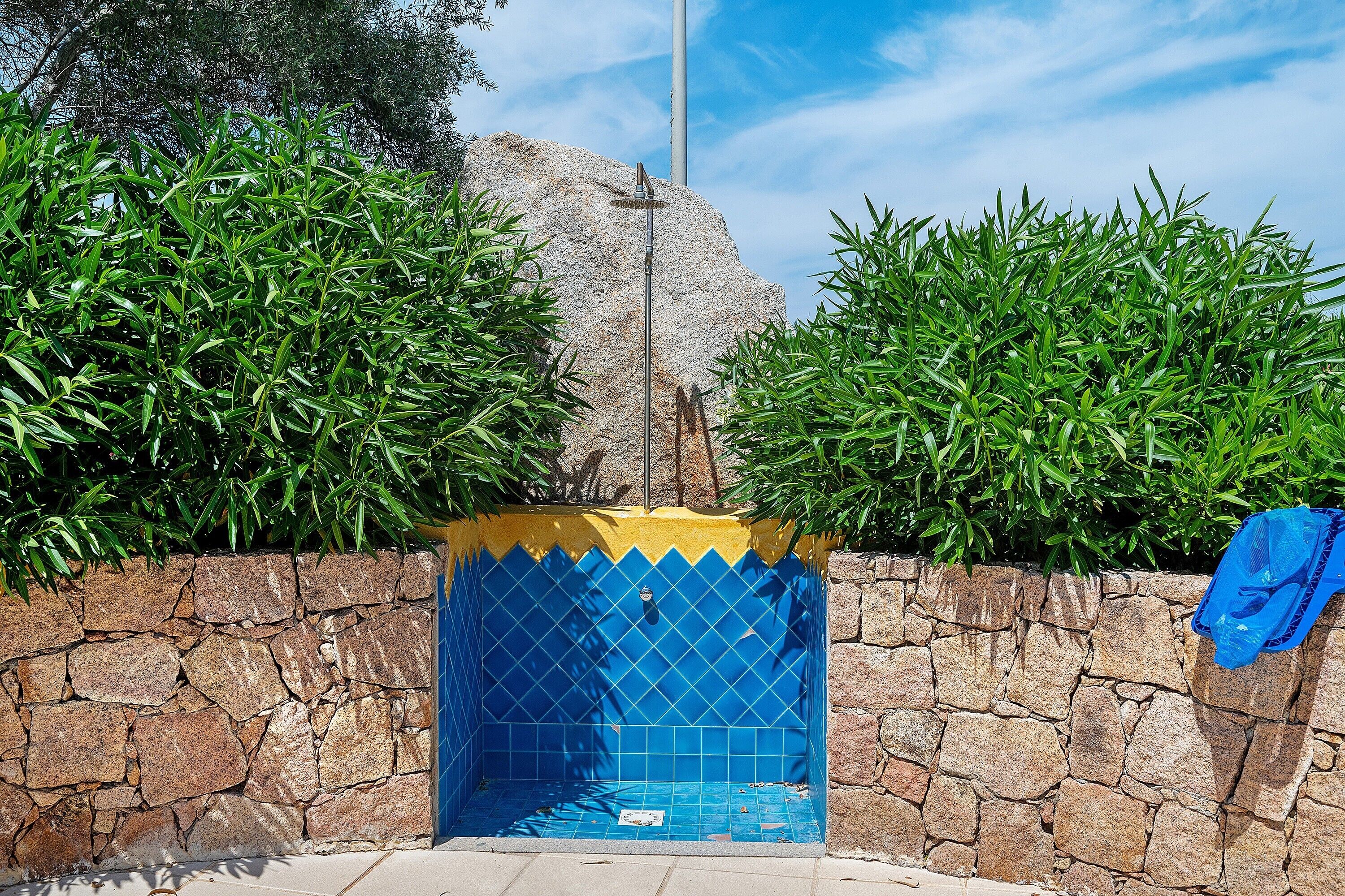 Un mur de pierre bordant un espace piscine agrémenté de carreaux bleus, le tout entouré de verdure.