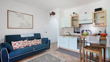 En kompakt opholdsstue med sofa, spisebord og et tekøkken.