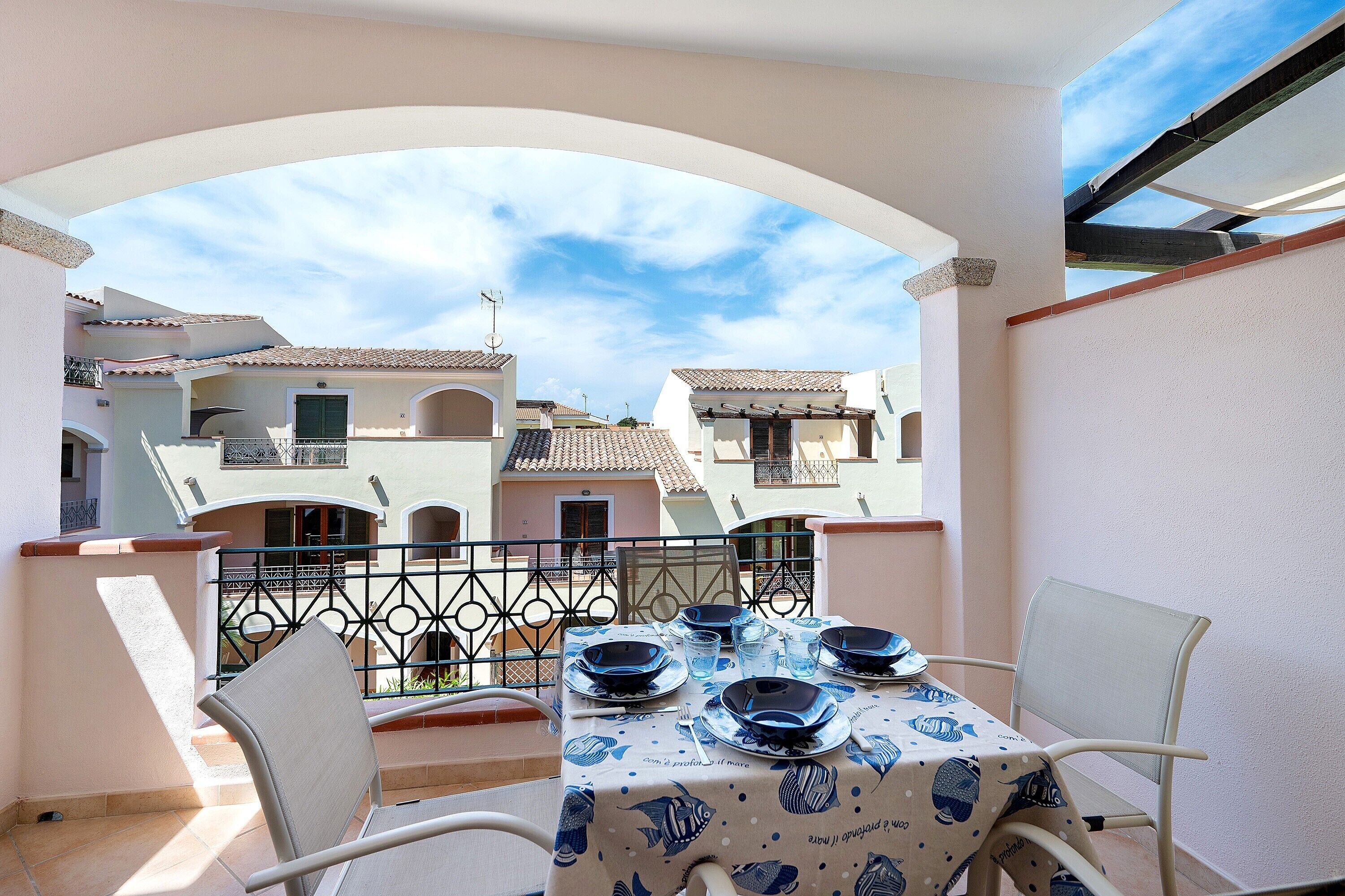 Un balcon avec une table dressée pour le dîner, des chaises blanches et une vue sur les bâtiments voisins.
