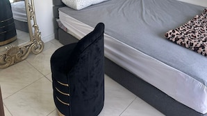 Un dormitorio con cama, un espejo grande, una silla negra y una lámpara fijada a la pared.