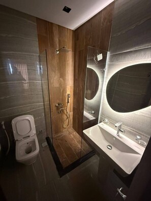 Et moderne badeværelse med en brusekabine i glas, toilet og et stort spejl over en vask.