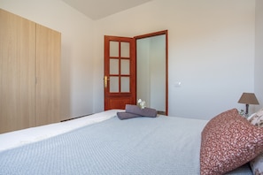 A bedroom with a bed, a wooden wardrobe, a door with glass panels, and a bedside table with a lamp. - Apartment Antonia: Private Terrace, Balcony & Air Conditioning in Betancuria (Betancuria)
