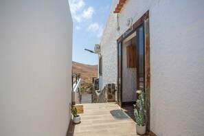 A narrow outdoor corridor with a stone staircase leading to a door, potted plants, and a view of a mountainous landscape.