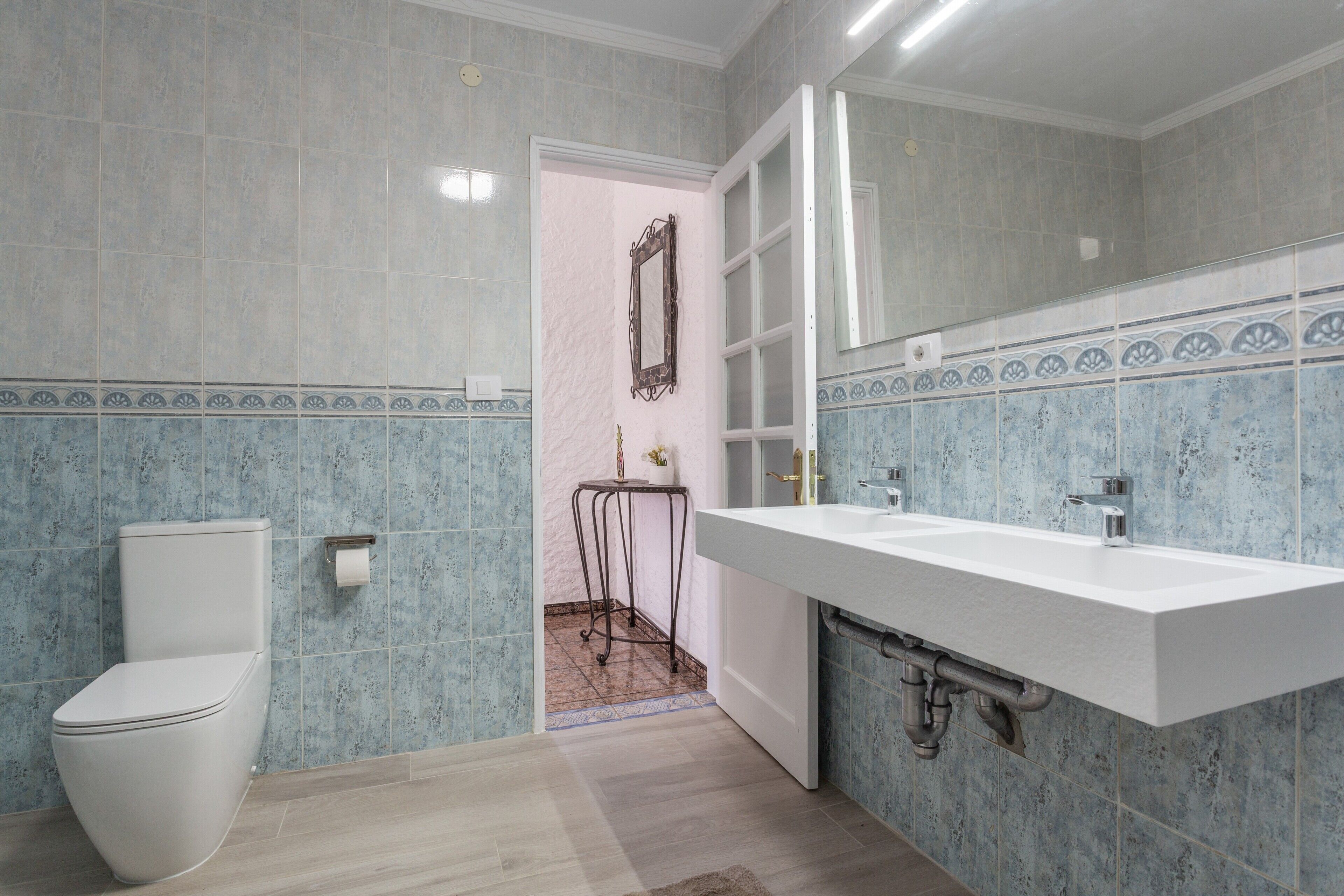 Un baño con inodoro, lavamanos, espejo y paredes con azulejos.