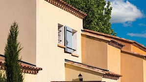 Ein Gebäude mit einer beige farbenen Fassade, einer Holz-Pergola und einer Tür mit einer Hausnummer.