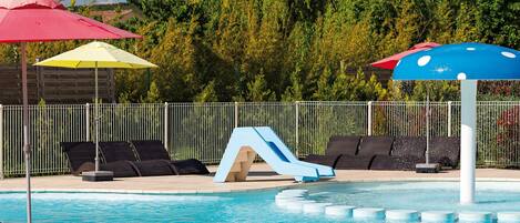 A swimming pool with lounge chairs and umbrellas, surrounded by a fence and trees.