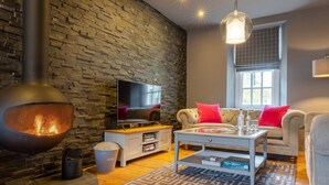 Ein gemütliches Wohnzimmer mit Steinwand, Fernseher, Kamin, Sofa und Couchtisch.