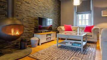 Una sala de estar acogedora con pared de piedra, televisor, chimenea, sofá y mesa de centro.
