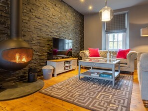 A cozy living room with a stone wall, a TV, a fireplace, a sofa, and a coffee table. - Prospect House (Windermere)
