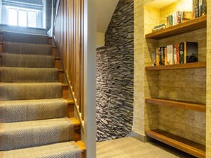 Uma escadaria com carpete texturizado, parede de pedra e uma estante com livros e uma fotografia emoldurada.