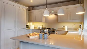 Una cocina moderna con gabinetes blancos, una isla central, iluminación colgante y una estufa a gas.