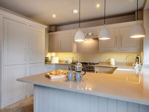 A modern kitchen with white cabinets, a central island, pendant lighting, and a gas stove. - Prospect House (Windermere)