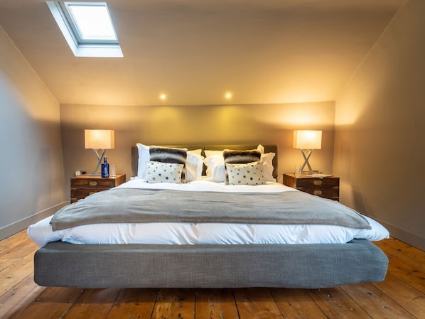 Ein Schlafzimmer mit einem großen Bett, zwei Nachttischen, einem Oberlicht und einem Holzboden.