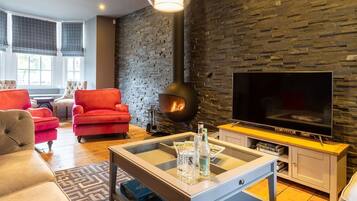 Una sala de estar moderna con una pared de piedra, una chimenea, un televisor y sillones rojos.