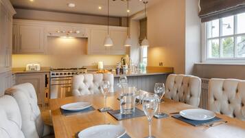 A modern kitchen with a dining area, featuring a wooden table set for six, a chandelier, and built-in appliances.