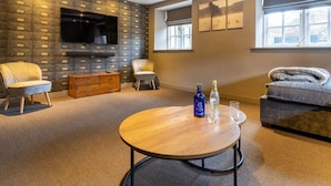 Ein modernes Wohnzimmer mit Steinwand, Flachbildfernseher, Holztisch und einer Couch.