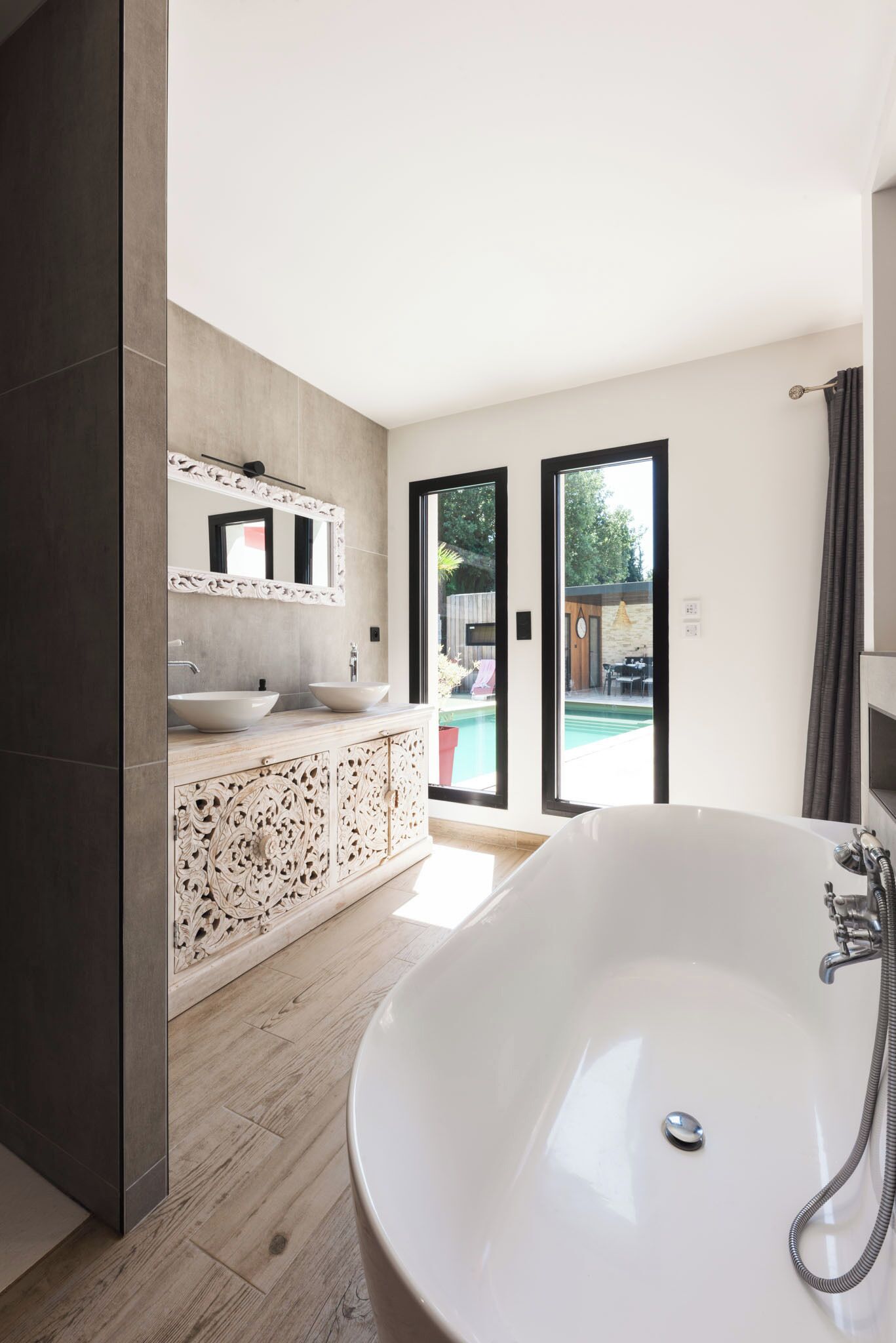 A modern bathroom with a large bathtub, two sinks, and a decorative cabinet.