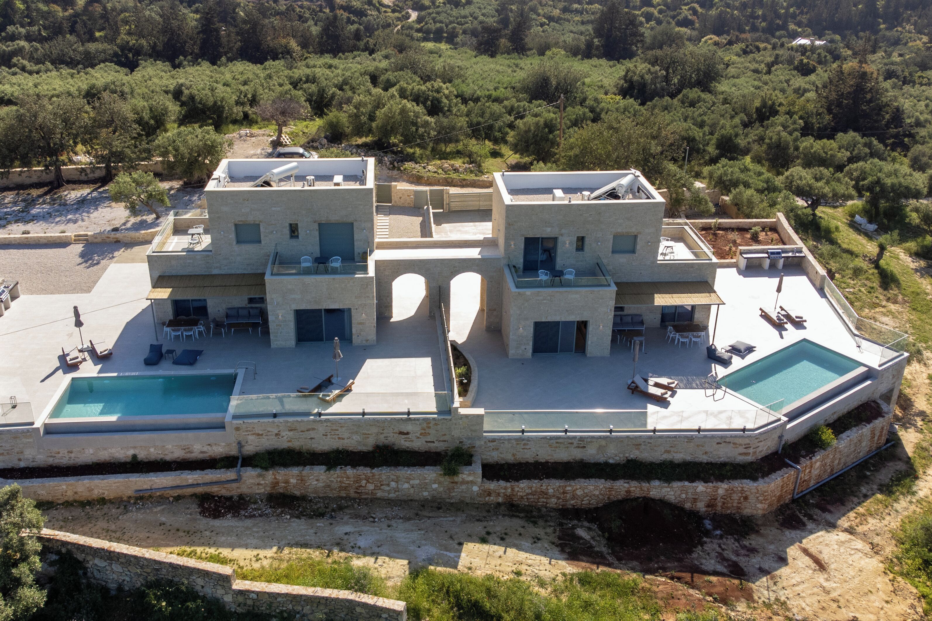 A modern villa with a swimming pool, outdoor seating, and a view of the surrounding forest.