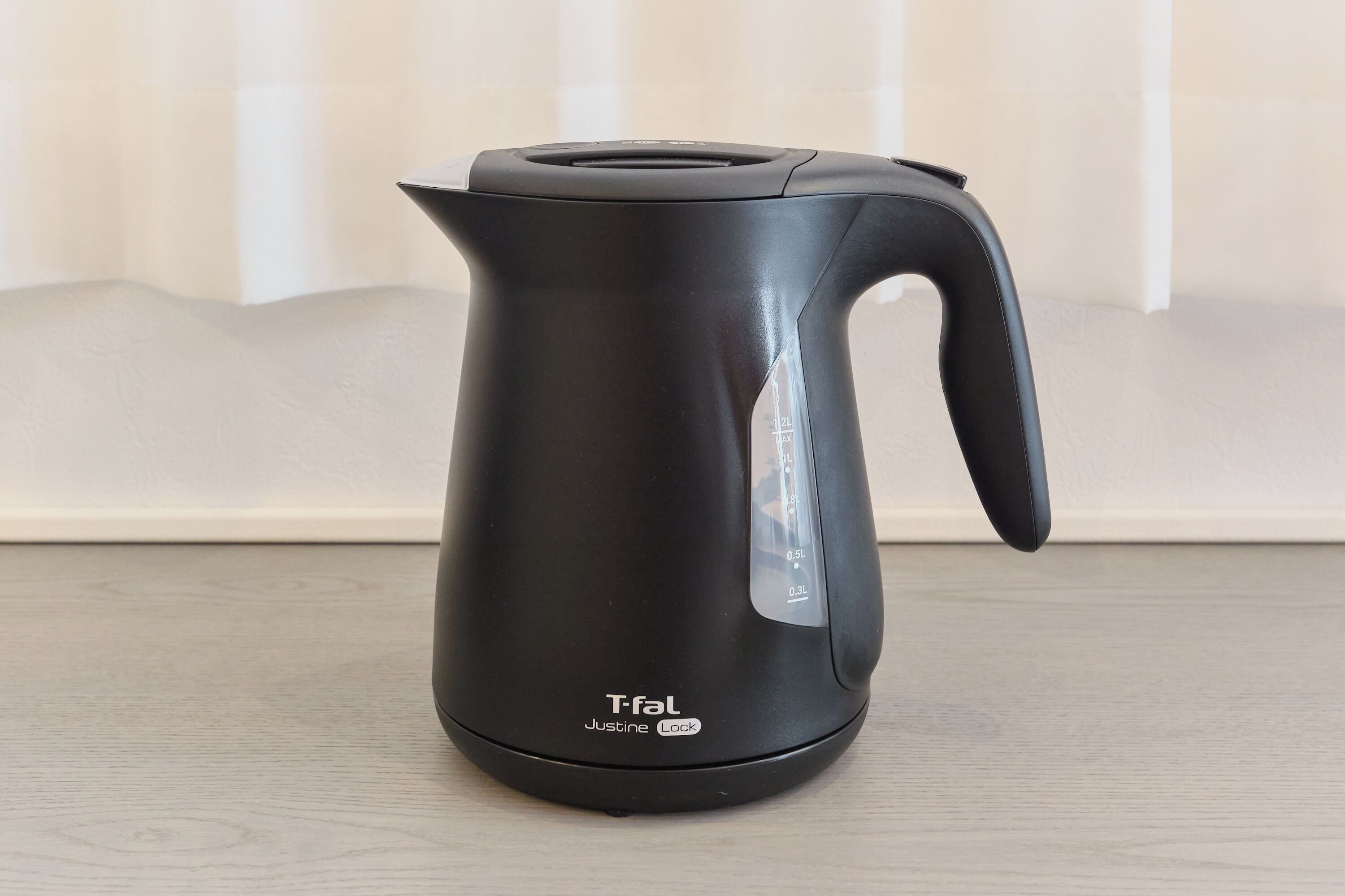 A black electric kettle with a handle and a spout, labeled 'T-fal Justine Lock,' on a wooden surface.