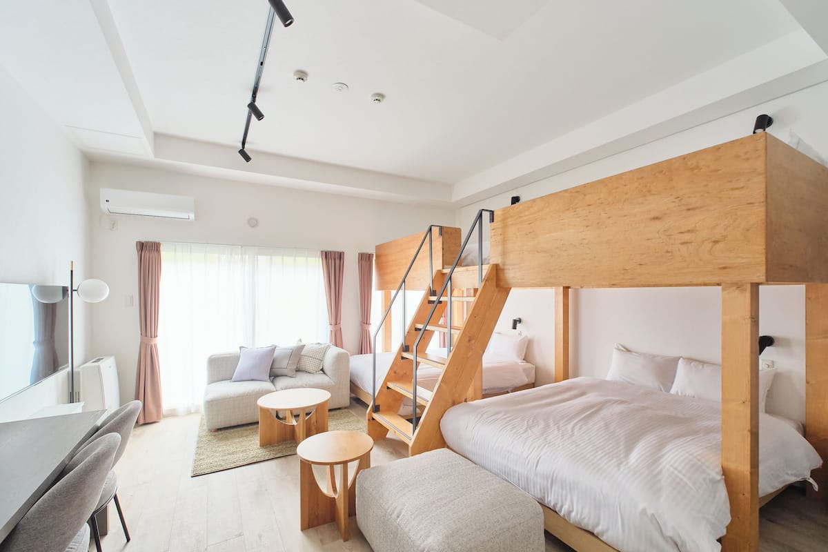 A modern hotel room with a bunk bed, a sofa, a desk, and a staircase.
