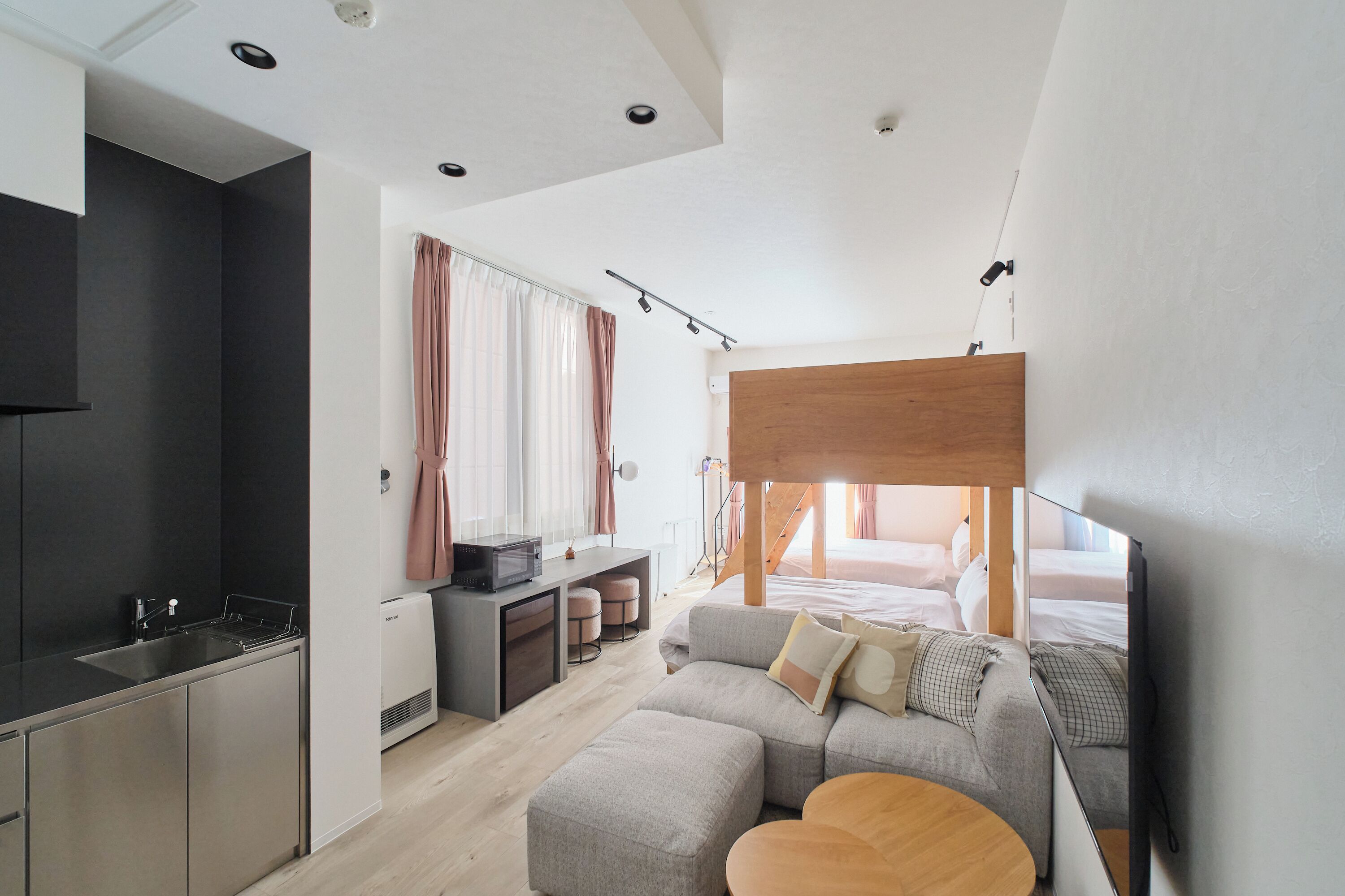 A modern hotel room with a kitchenette, a sofa, a wooden ceiling, and a bed.