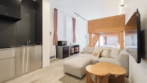 A modern kitchen with built-in appliances, a dining area with a wooden table, and a living space with a sofa and a TV mounted on the wall.