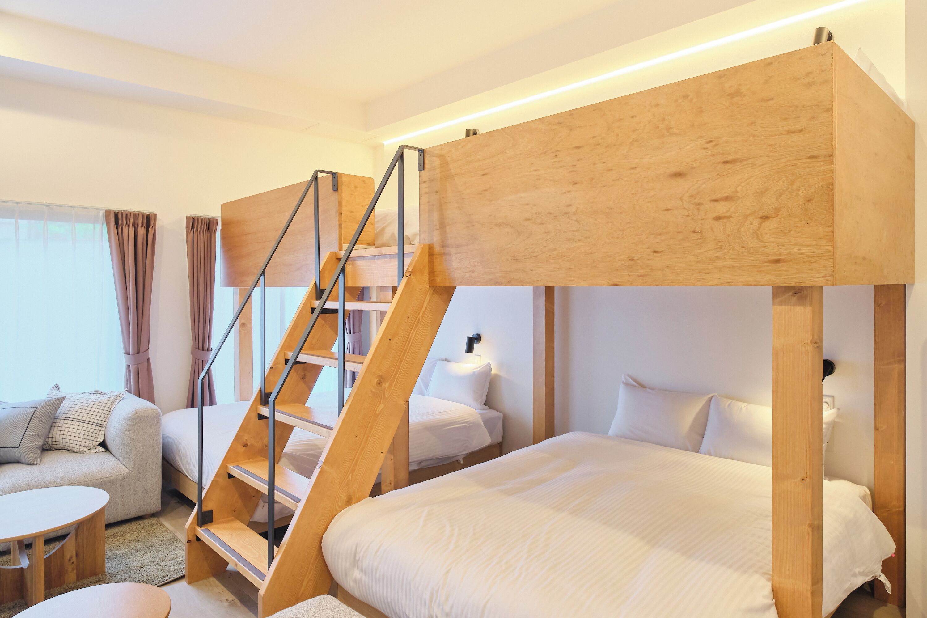 Una habitación de hotel moderna con una cama litera, un sofá, una mesita y una escalera.
