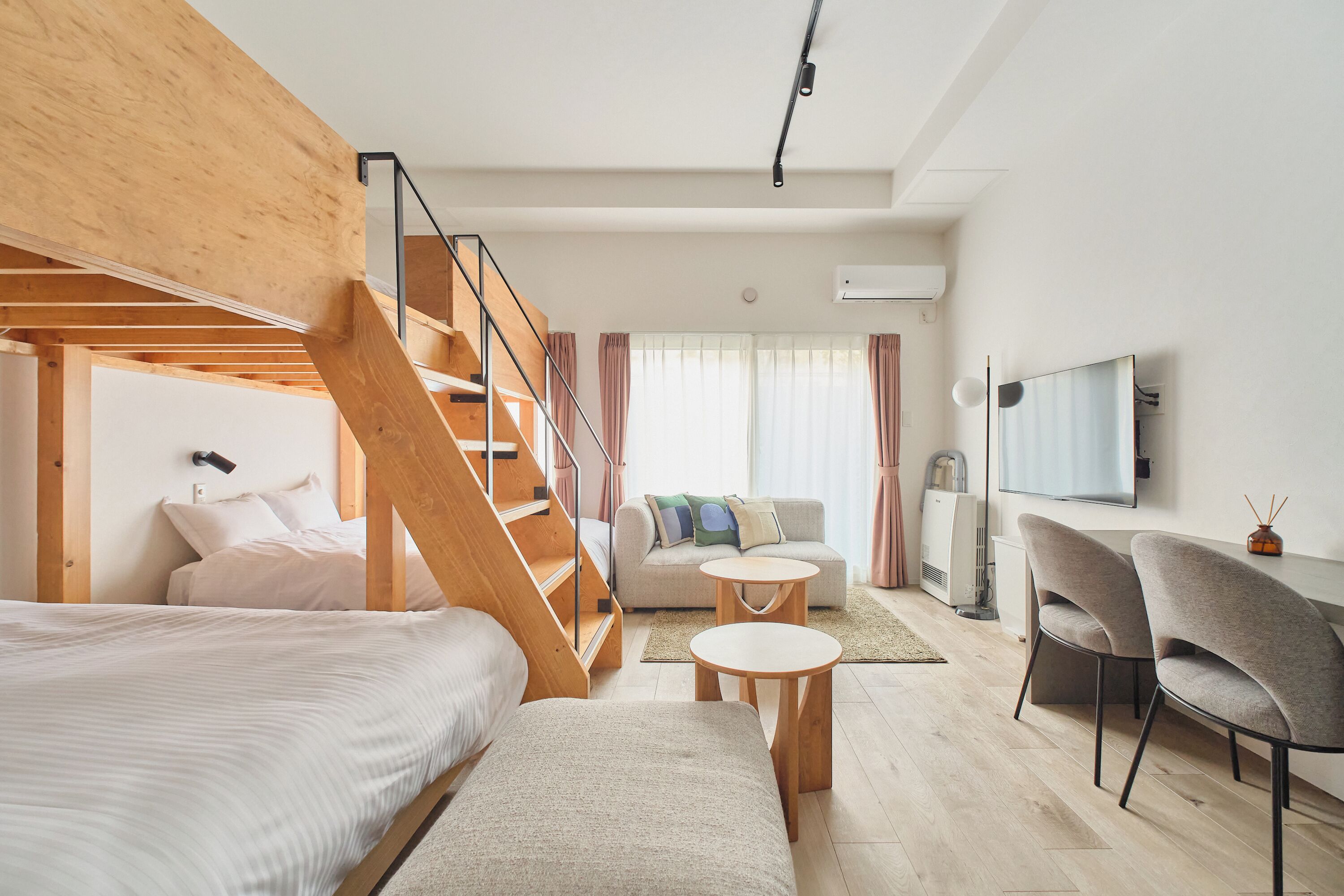 A modern hotel room with a wooden staircase, a sofa, a bed, a small round table, and a TV.