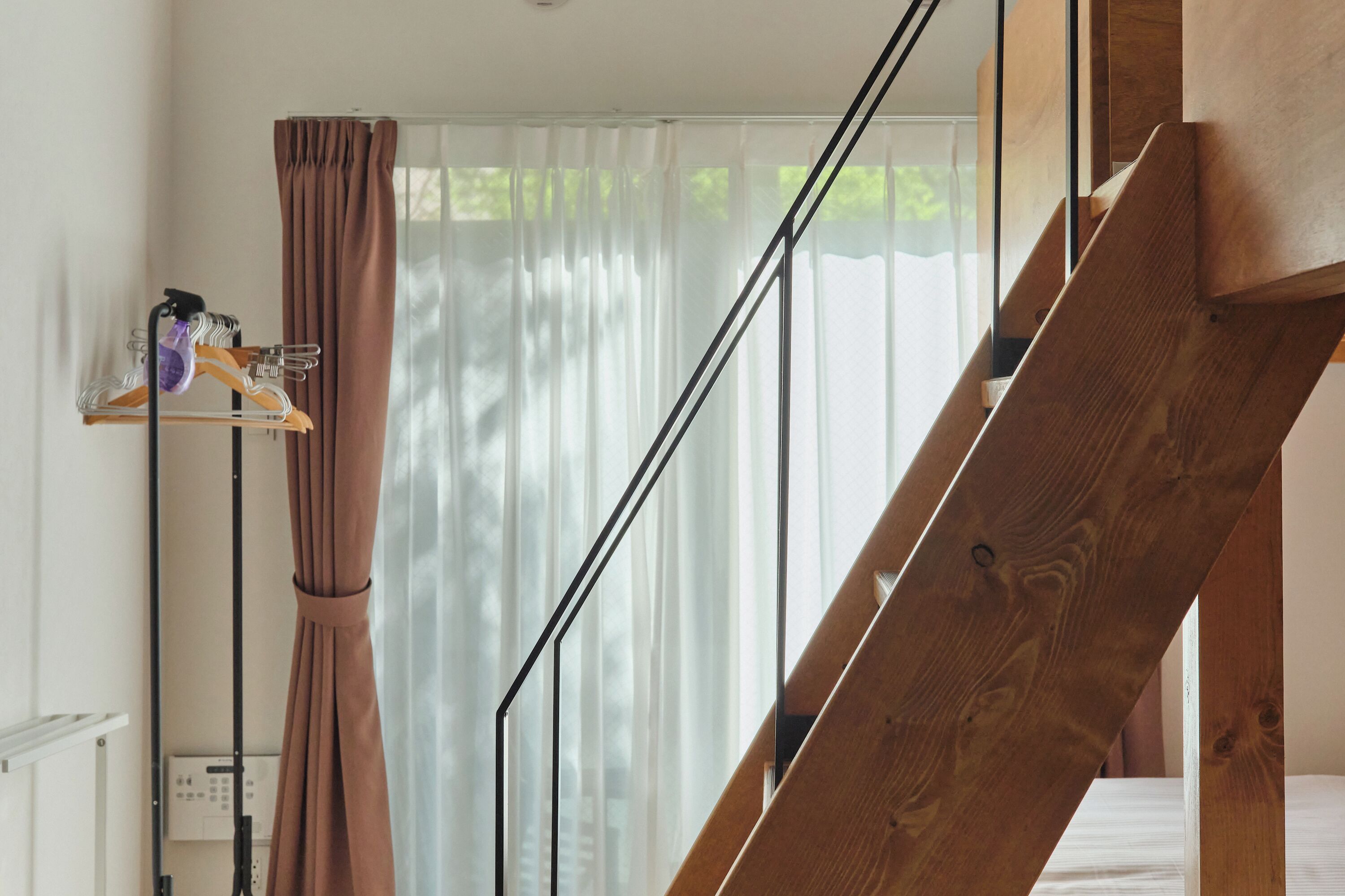 A staircase with wooden railings, a curtain, and a clothing rack with hangers and a bottle.