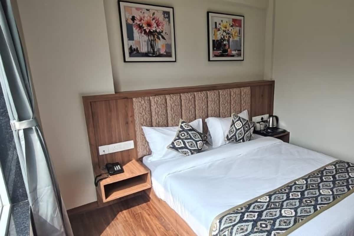 Ein Hotelzimmer mit einem Bett, einem Nachttisch, einem Holzkopfstück und zwei an der Wand hängenden Blumenbildern.
