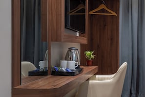 A wooden table with a coffee maker, cups, and a tray with snacks. A potted plant is on the table, and a chair is visible. - Monarch Montvert Hitec (Hyderabad)
