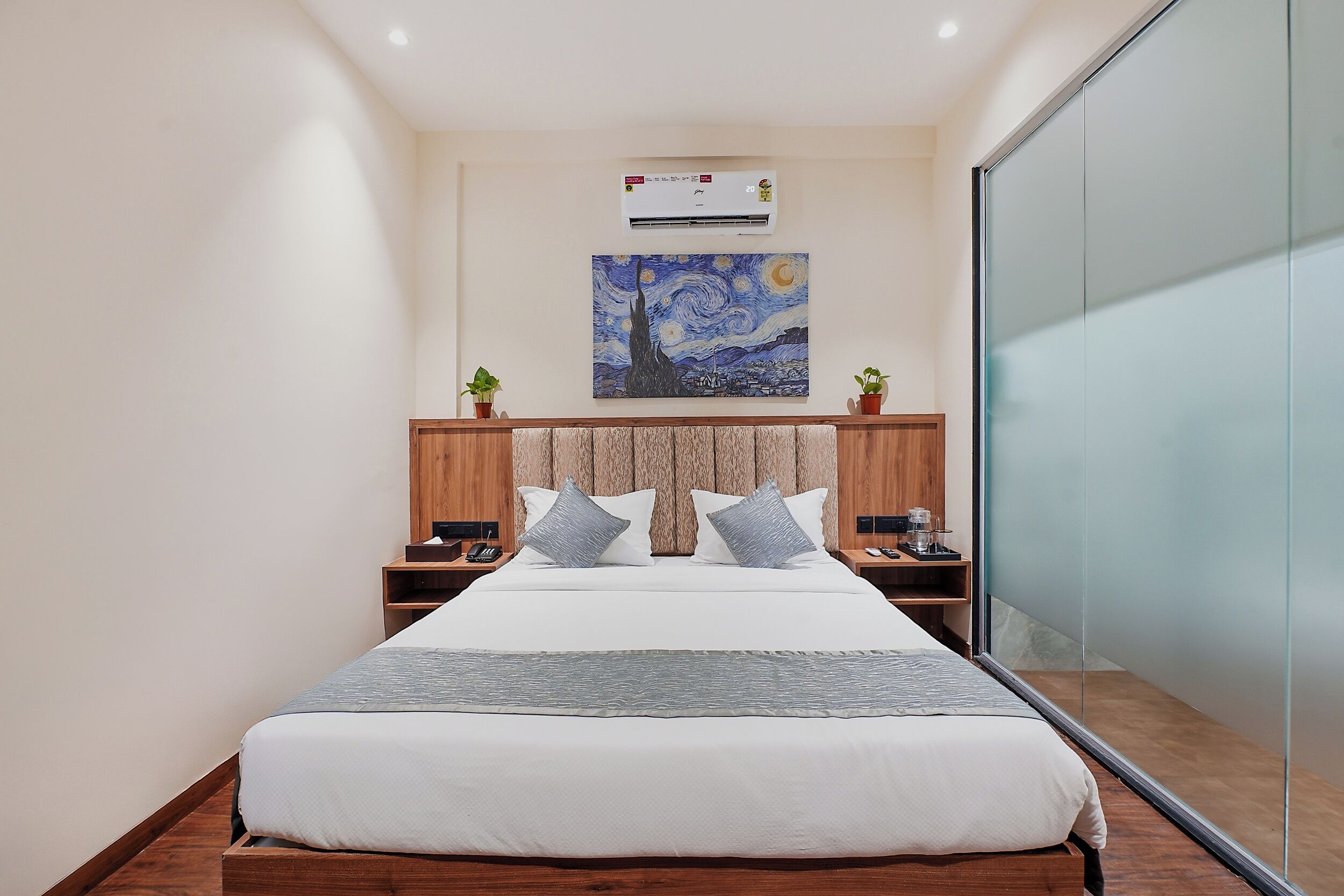 Habitación de hotel con cama, mesitas de noche, aire acondicionado, un cuadro en la pared y una puerta corrediza de vidrio.