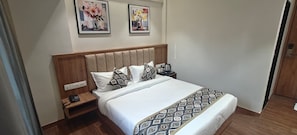 A hotel room with a bed, bedside table, and two framed pictures on the wall. - Monarch Montvert Hitech (Hyderabad)