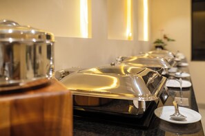 A buffet setup with covered food containers and a spoon on a plate.