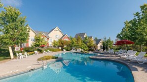 En swimmingpool med solstolar och parasoller, omgiven av byggnader i traditionell arkitektonisk stil.