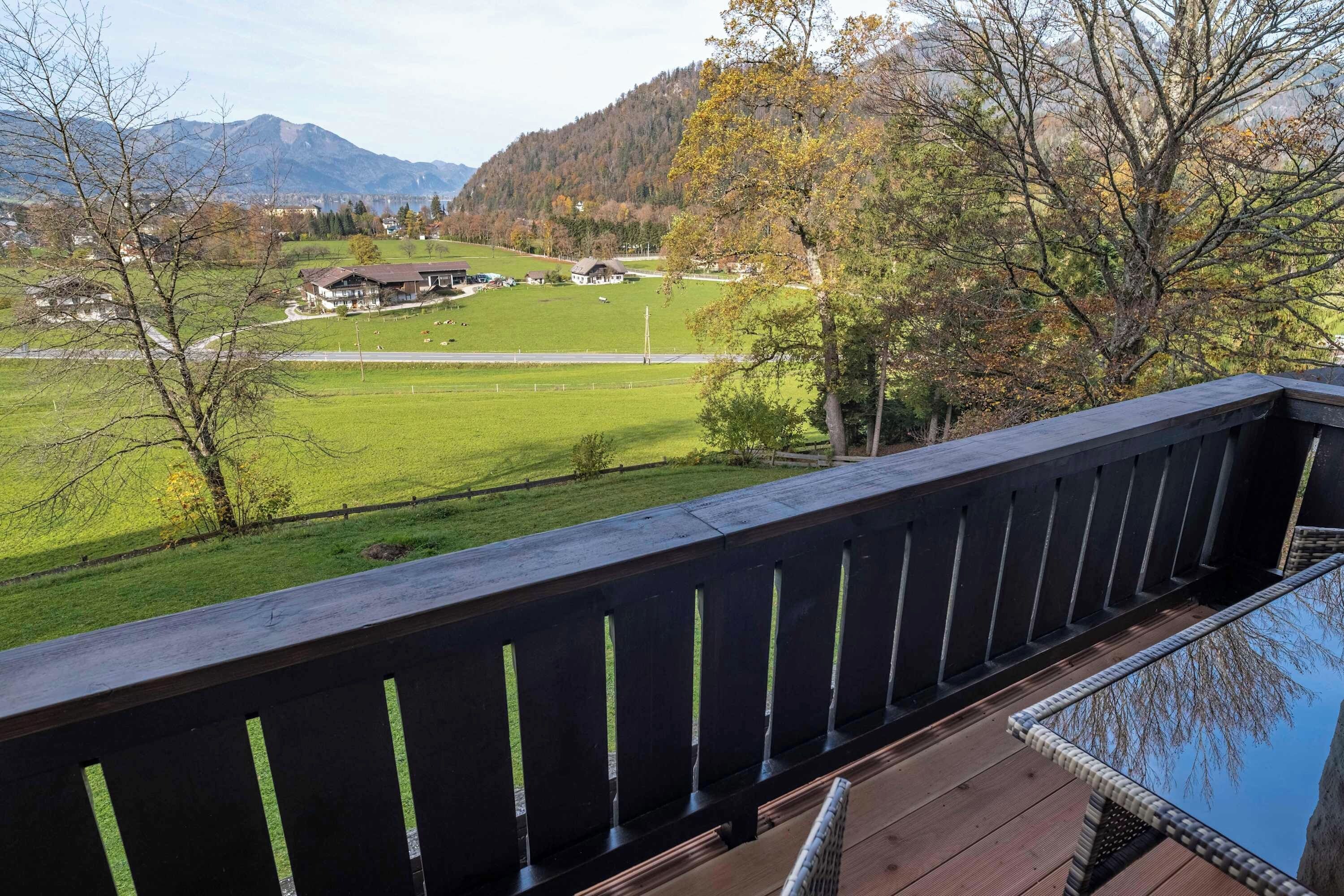 Eine Holzterrasse mit Blick auf ein grünes Feld, ein Haus und Berge in der Ferne.