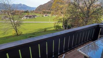 Eine Holzterrasse mit Blick auf ein grünes Feld, ein Haus und Berge in der Ferne.