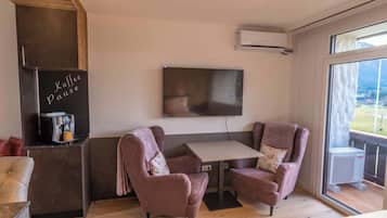 A modern room with a sofa, a small table, a coffee machine, and a TV mounted on the wall.