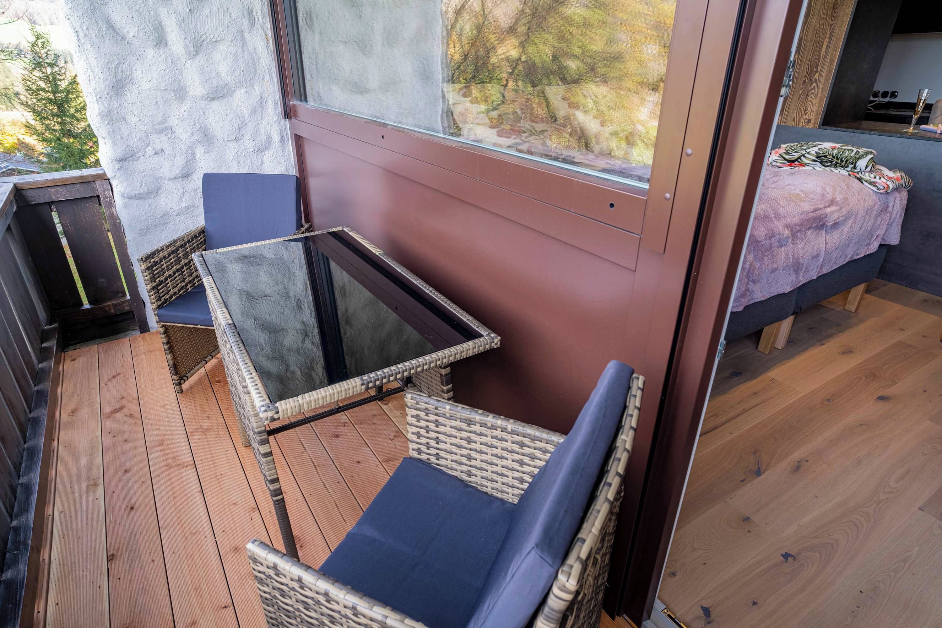 Un balcon agrémenté de meubles en osier, d’une table en verre et d’un lit recouvert d’une couverture violette.