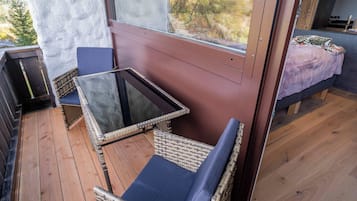 Un balcon agrémenté de meubles en osier, d’une table en verre et d’un lit recouvert d’une couverture violette.