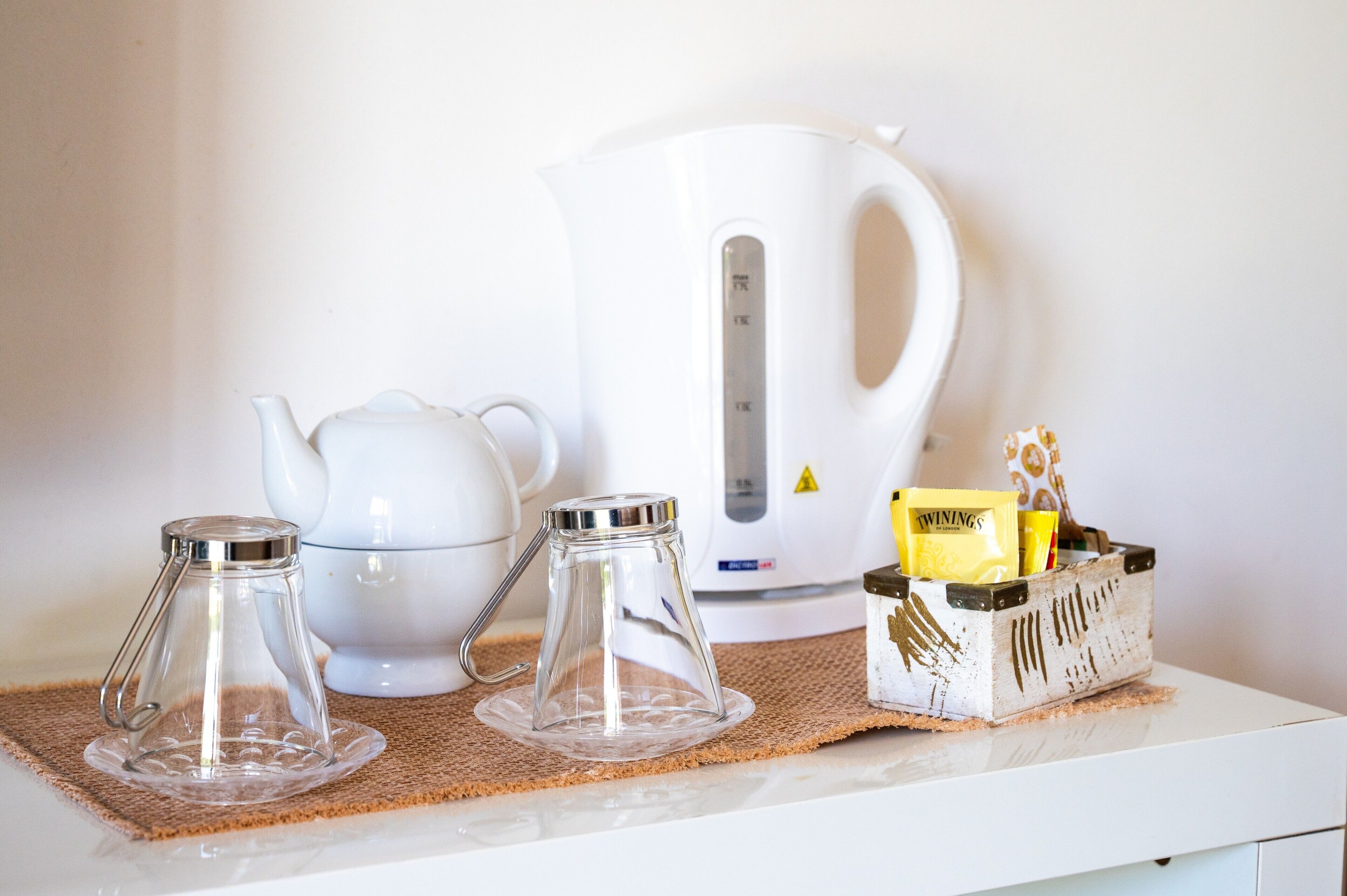 A kitchen area with a white kettle, two glass carafes, and a container with Twinings tea bags.