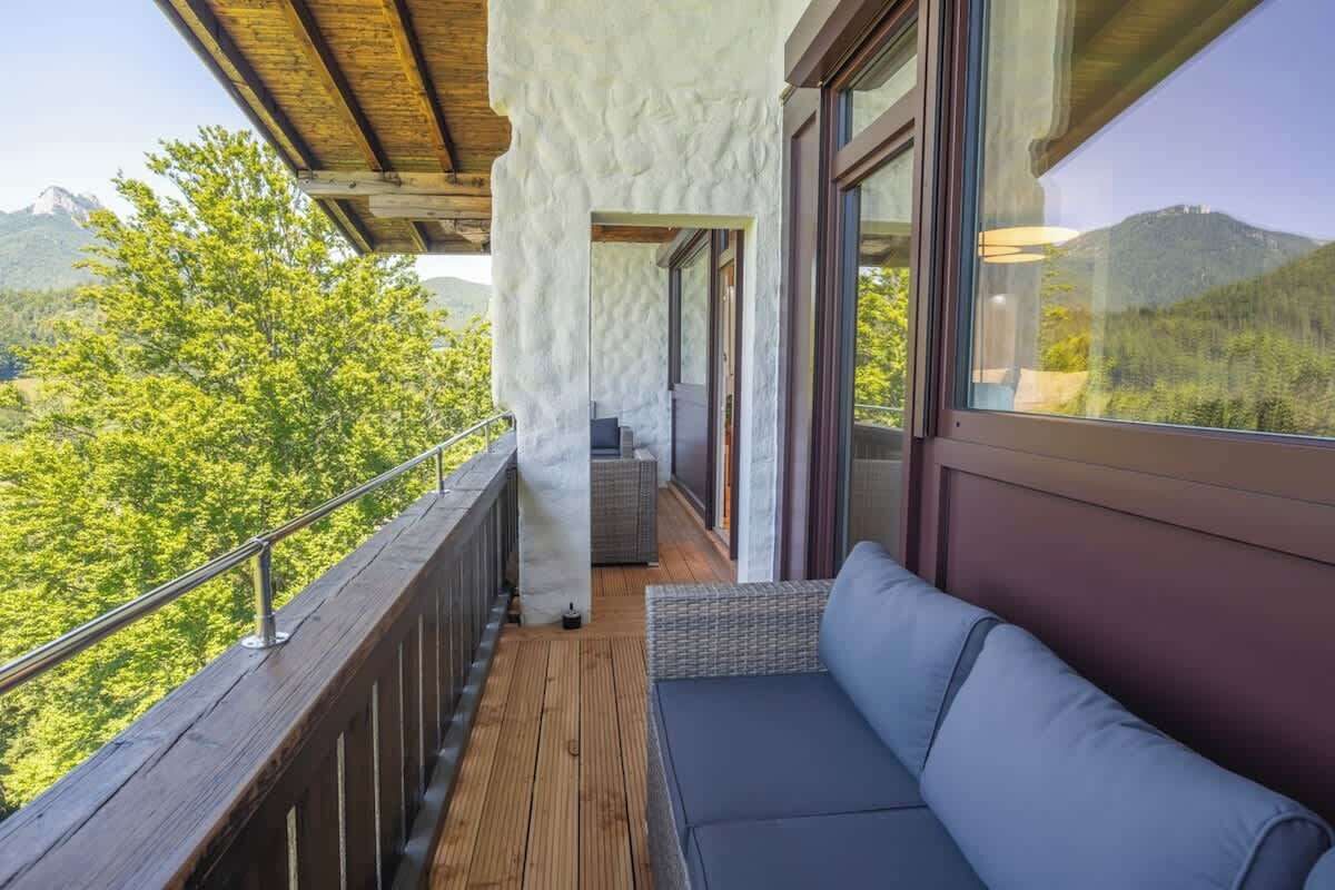 Un balcon doté d’un plancher en bois, d’un espace salon avec des coussins et offrant une vue sur un paysage montagneux.