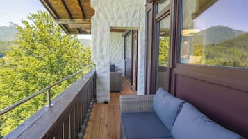 Un balcon doté d’un plancher en bois, d’un espace salon avec des coussins et offrant une vue sur un paysage montagneux.